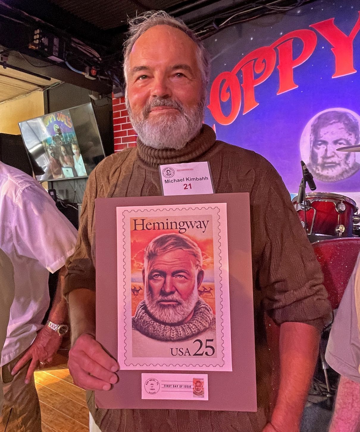 Michael Kimbahh hält ein vergrößertes Faksimile einer Ernest Hemingway-Briefmarke in der Hand, um seine Ähnlichkeit beim Hemingway Look-Alike Contest zu demonstrieren.
